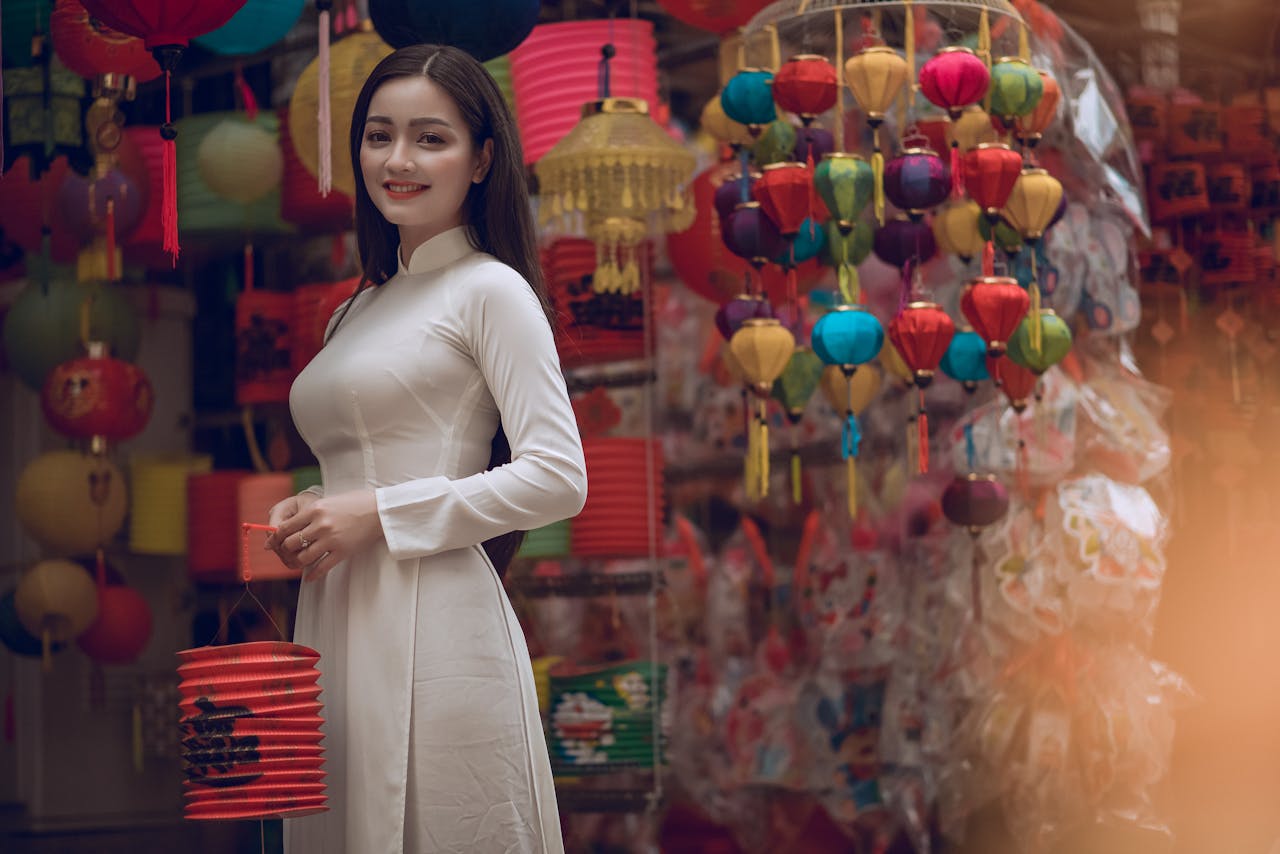 A joyful Asian woman holding colorful lanterns in a lively outdoor market setting.