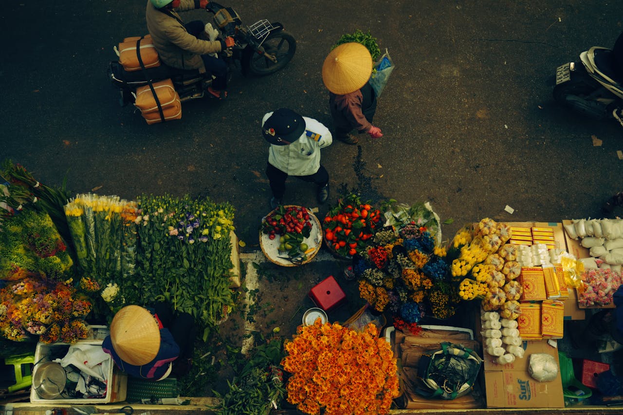 heros-img A bustling street market scene with people and colorful flowers viewed from above.